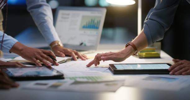 Business professionals analyze financial data and graphs in an office, discussing investment strategies.