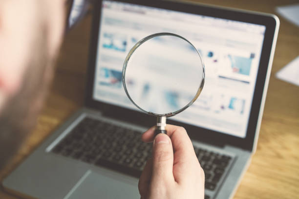 Person using magnifying glass to examine online business opportunities displayed on a laptop screen.