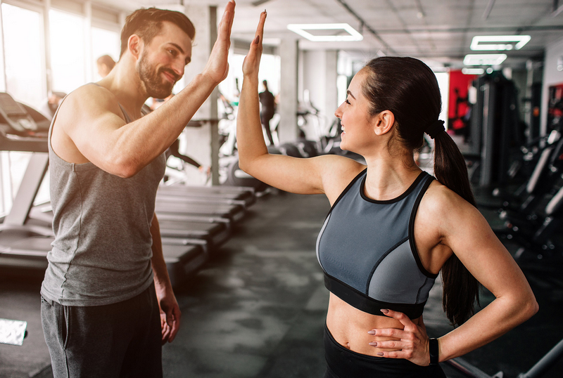 A man and woman give each other a high-five in a gym.