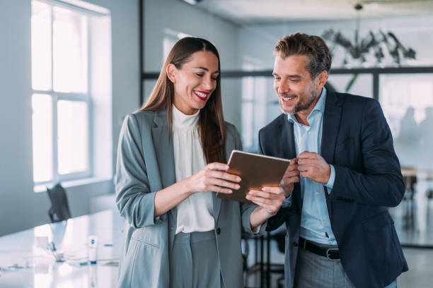 Two business professionals discuss strategies on a tablet in an office to save licensing costs in RAK Free Zone.